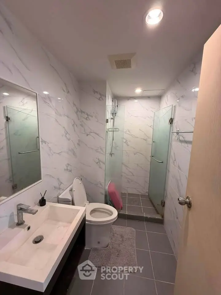 Modern bathroom with sleek fixtures and marble walls, featuring a glass-enclosed shower and stylish vanity.