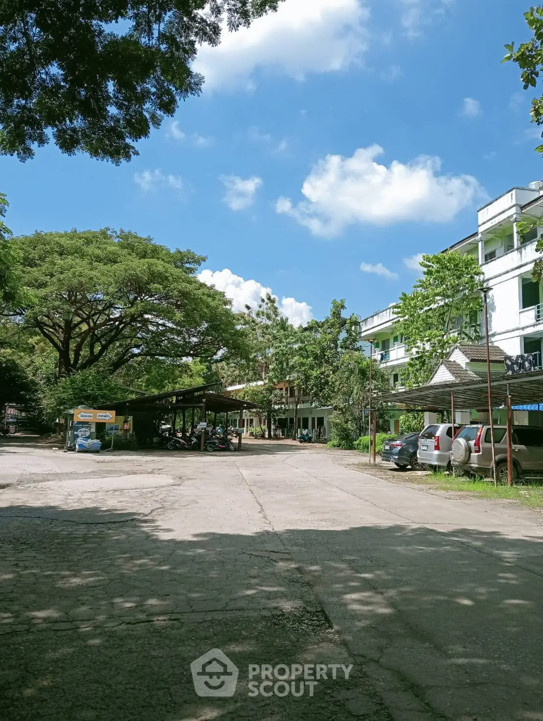 Charming residential building with lush greenery and spacious parking area under a clear blue sky.