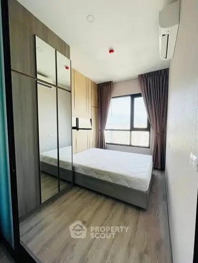 Modern bedroom with large window and mirrored wardrobe in high-rise apartment.