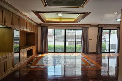 Spacious living room with wooden built-in cabinets and large windows overlooking garden
