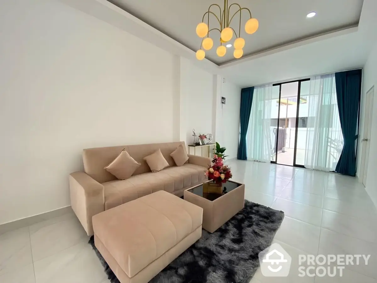 Elegant living room with plush beige sofa set, chic pendant lighting, and access to a sunlit balcony, perfect for modern living.