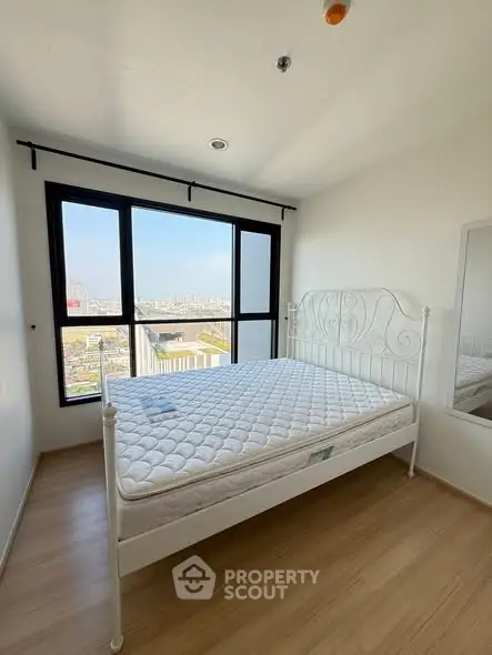 Bright bedroom with large window offering stunning city views, featuring a stylish metal bed frame and wooden flooring.