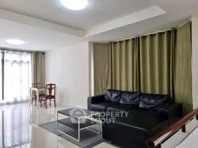 Spacious living room with modern black leather sofa and elegant dining area, perfect for entertaining.