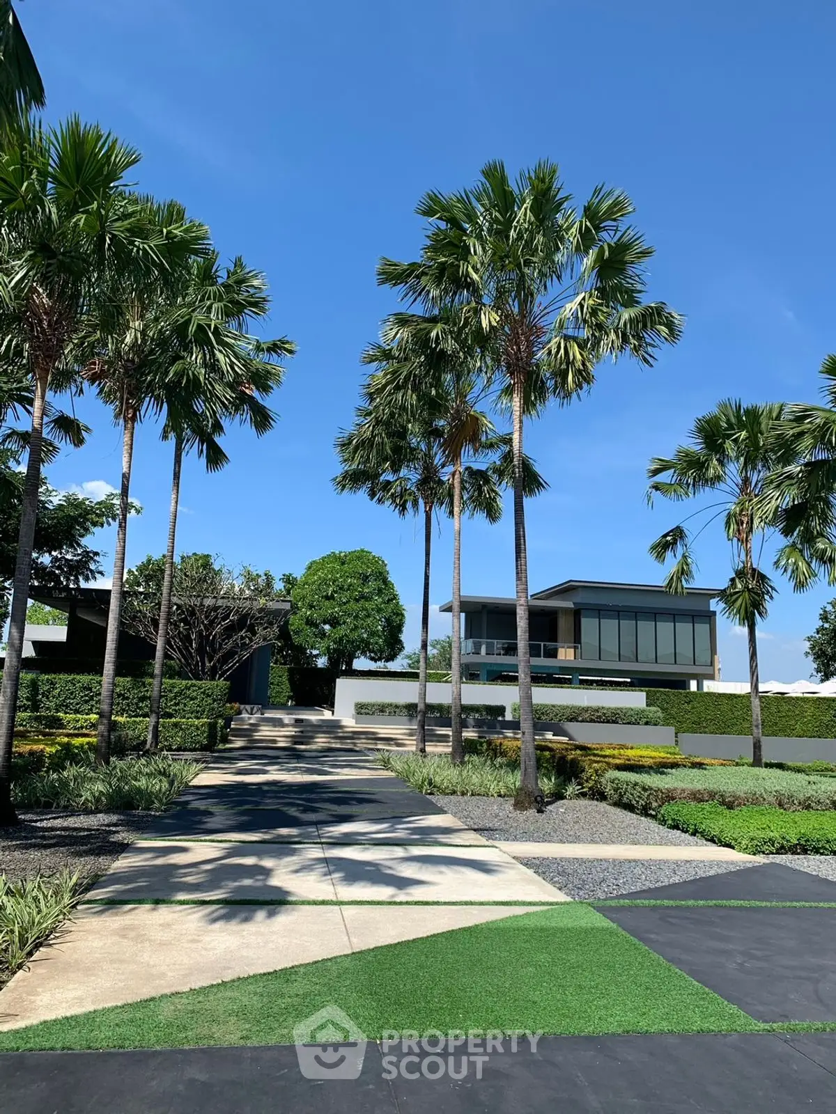 Luxurious modern home with lush landscaping and palm trees under a clear blue sky.