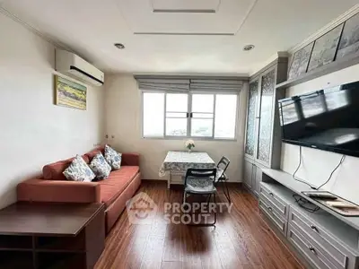Cozy living room with sofa, TV, and dining area, featuring wooden flooring and natural light.