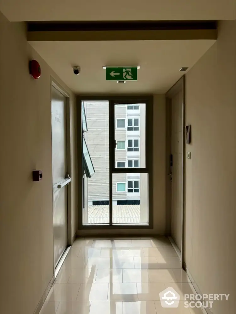 Bright apartment hallway with emergency exit sign and large window view