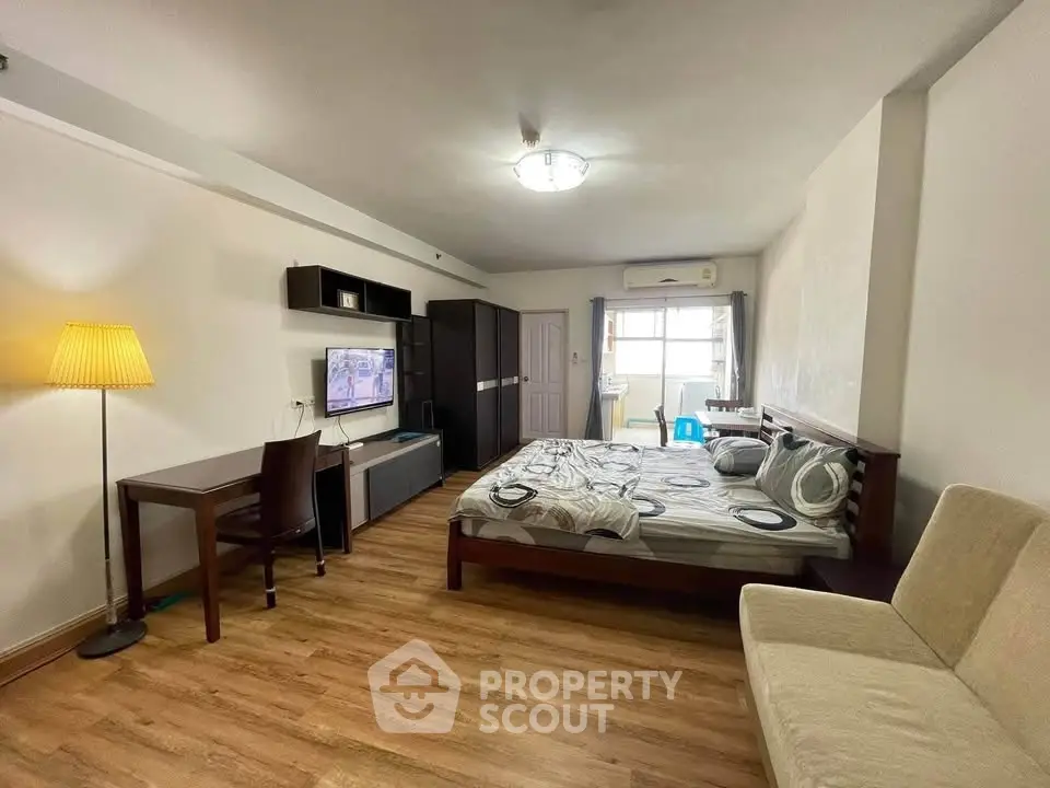 Spacious studio apartment with modern furnishings and wooden flooring, featuring a cozy bed and ample natural light.