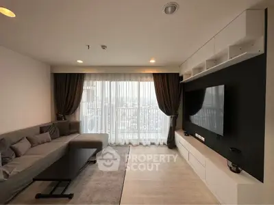 Modern living room with large TV and city view balcony, elegant decor and ample natural light.