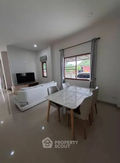 Modern living room with dining area, featuring sleek furniture and large windows for natural light.