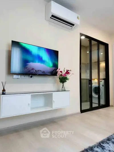 Modern living room with wall-mounted TV and air conditioner, featuring a glimpse of a laundry area.