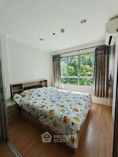 Bright bedroom with large window and wooden flooring, featuring a cozy bed with colorful bedding.
