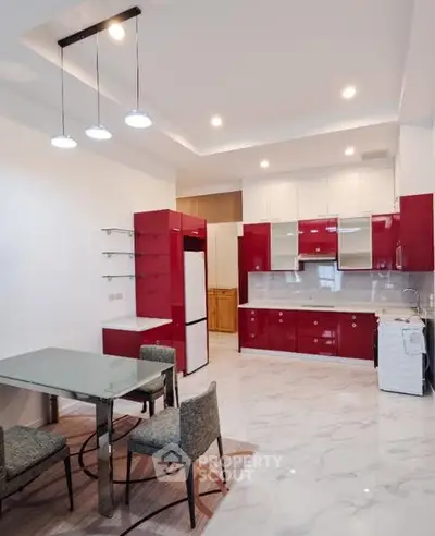 Modern kitchen with red cabinets, glass dining table, and sleek lighting in a spacious open layout.