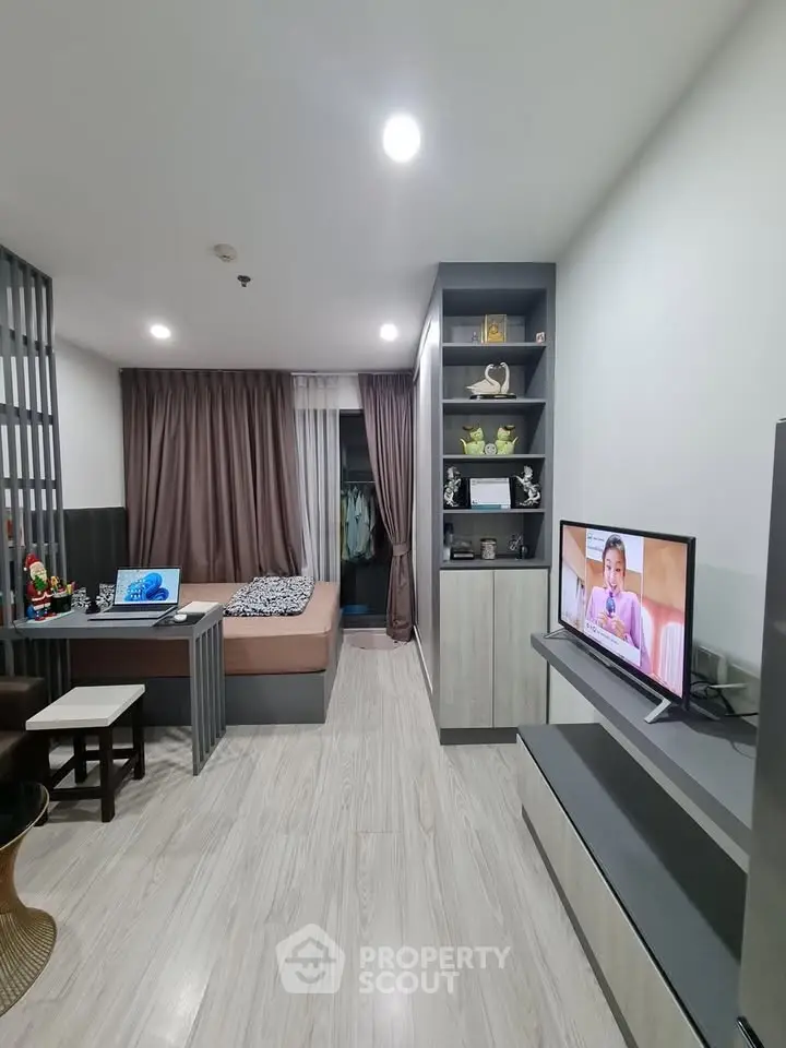 Modern studio apartment with sleek design, featuring a cozy bed, stylish shelving, and a wall-mounted TV.