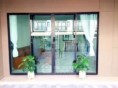 Modern balcony with sliding glass doors and potted plants, offering a view of neighboring buildings.