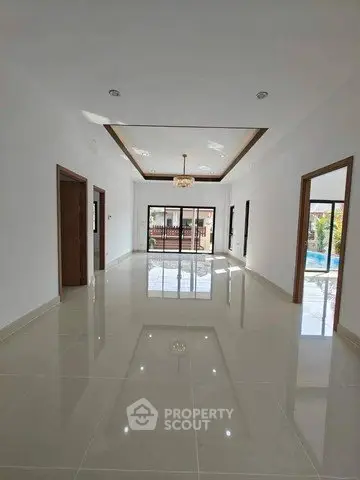 Spacious modern living room with elegant chandelier and large windows overlooking pool area.