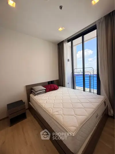 Modern bedroom with large window and balcony access, featuring a comfortable bed and stylish decor.