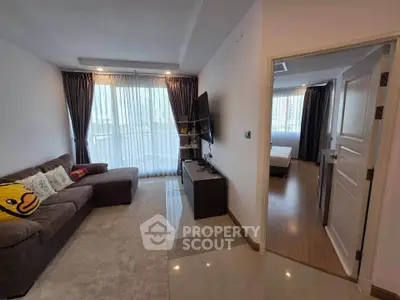 Modern living room with cozy sofa and TV, leading to a bright bedroom with large windows.