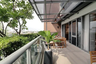 Spacious balcony with modern glass canopy and lush greenery, perfect for outdoor dining and relaxation.