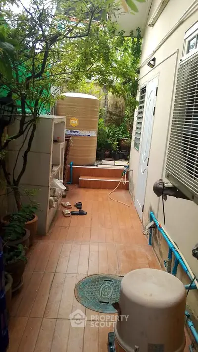 Charming outdoor corridor with lush greenery and utility area, perfect for urban gardening enthusiasts.