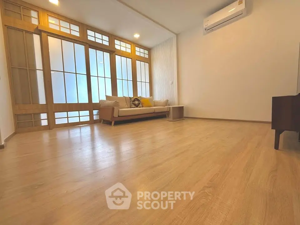 Spacious living room with wooden flooring and modern decor, featuring a cozy sofa and air conditioning.
