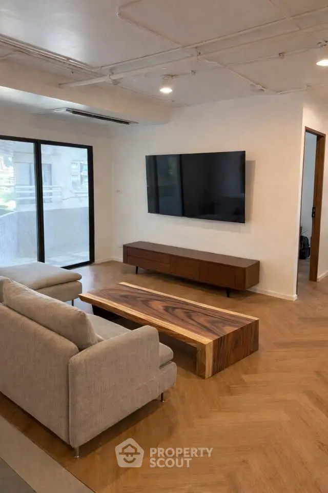 Modern living room with sleek furniture and large TV, featuring wooden flooring and natural light.