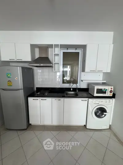 Modern kitchen with sleek white cabinets, washing machine, and stainless steel appliances.
