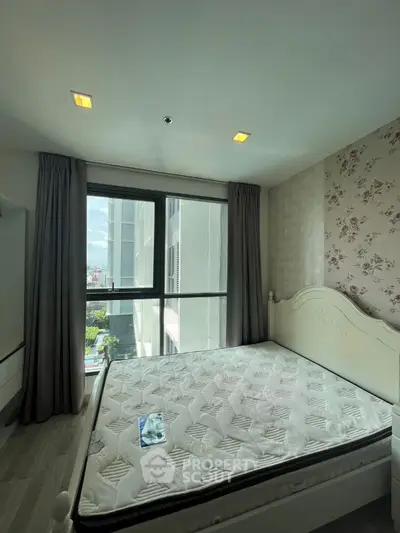 Bright bedroom with large window and floral wallpaper, featuring a comfortable bed and modern decor.
