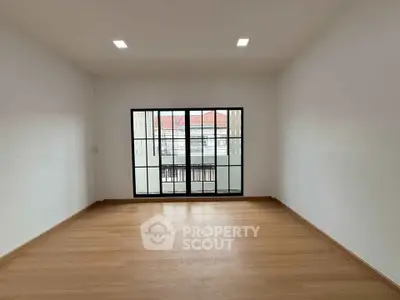Spacious empty room with large window and wooden flooring, perfect for customization.