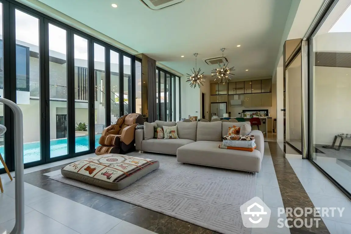 Luxurious open-plan living space with plush sofas and modern decor, floor-to-ceiling windows overlooking a private pool, seamlessly connecting to a sleek kitchen.