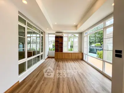 Spacious living room with large windows and wooden flooring, offering abundant natural light and a serene view.