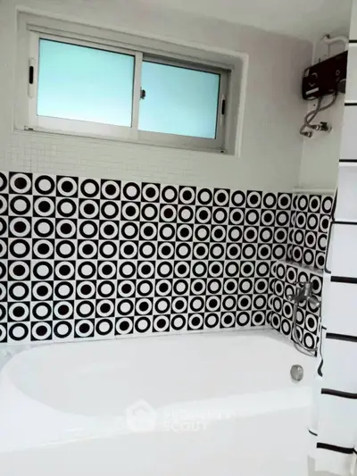 Stylish bathroom with modern black and white geometric tiles and bathtub.