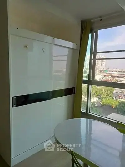 Bright corner unit with large window and city view, featuring a sleek white wardrobe and round dining table.
