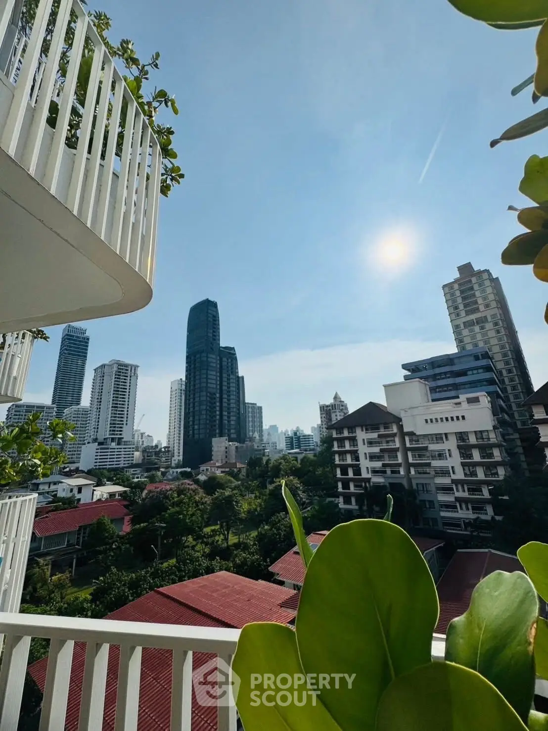 Stunning cityscape view from a modern balcony with lush greenery and high-rise buildings.
