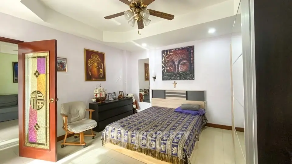 Spacious bedroom with artistic decor and ceiling fan, featuring a cozy bed and elegant stained glass door.