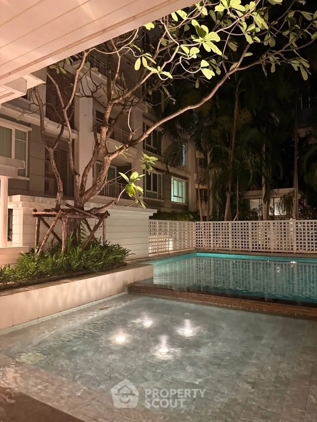 Luxurious night view of a serene residential pool surrounded by lush greenery.
