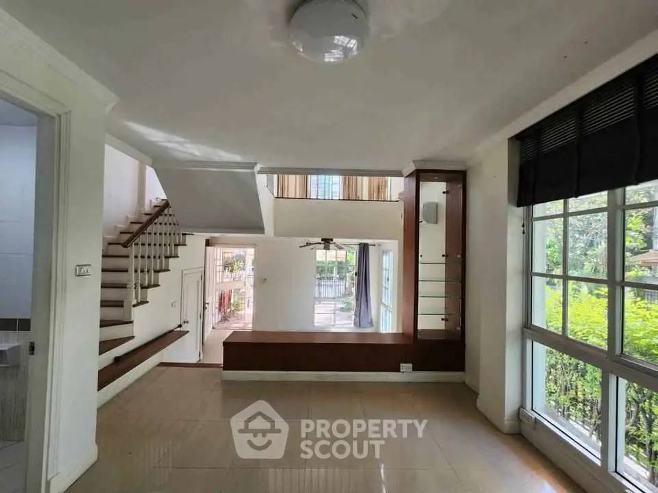 Spacious modern living room with large windows and elegant staircase, offering abundant natural light and garden views.