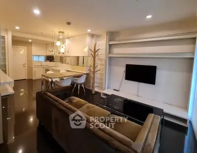 Modern living room with open kitchen, sleek furniture, and ambient lighting.