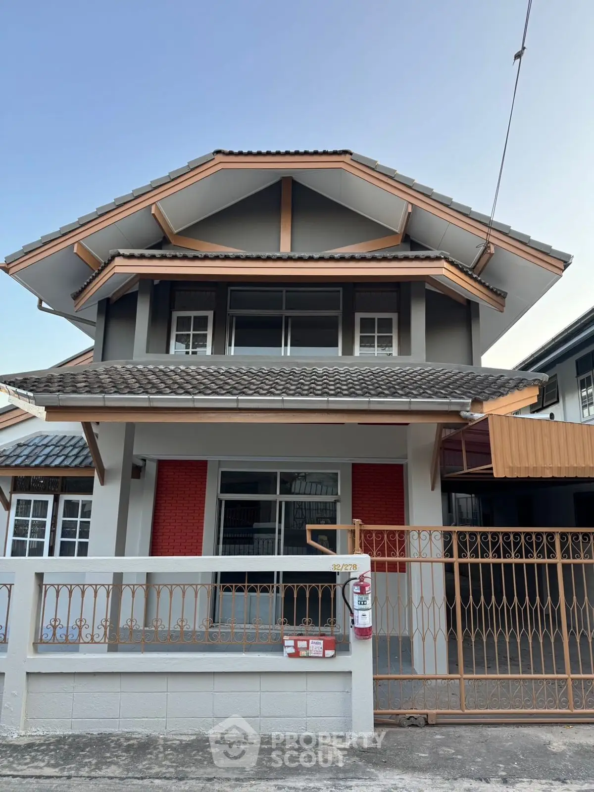 Charming two-story house with unique roof design and gated entrance in a serene neighborhood.