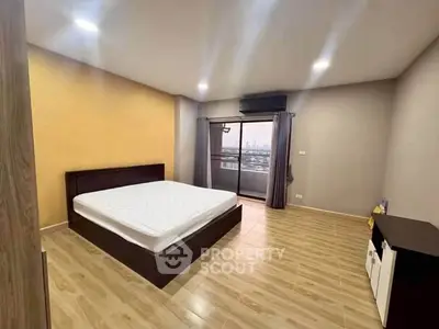 Spacious bedroom with balcony and city view, featuring modern decor and ample natural light.