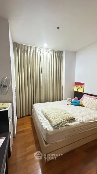 Cozy bedroom with wooden flooring and large window, featuring a comfortable bed and modern decor.