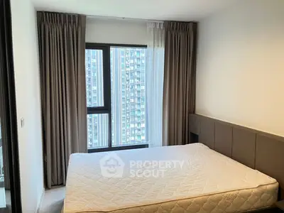 Modern bedroom with large window and city view, featuring neutral decor and comfortable bedding.