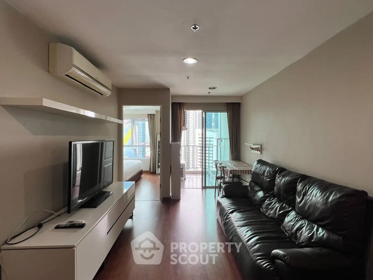Modern living room with sleek leather sofa and large TV, leading to a balcony with city views.