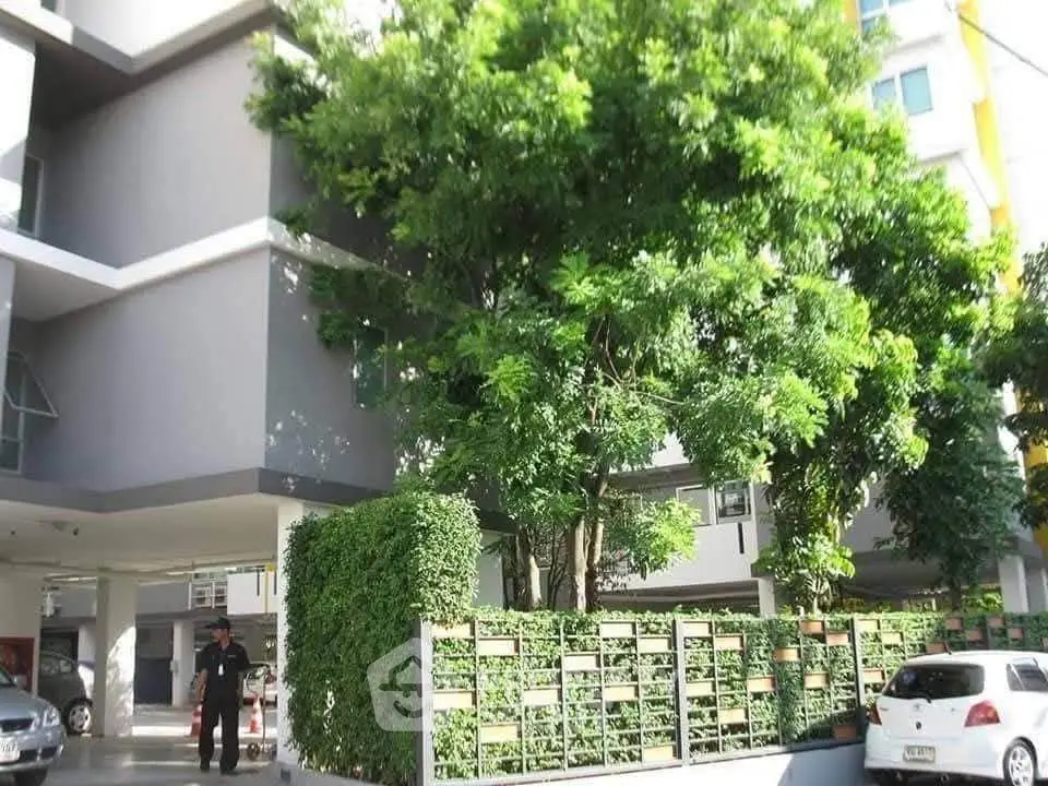 Modern apartment building exterior with lush greenery and parking area