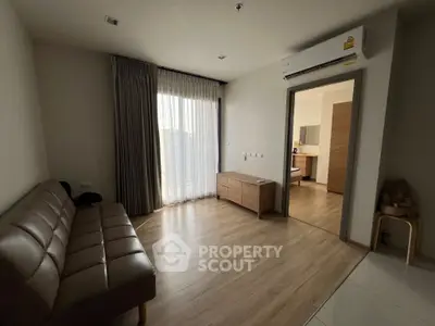 Modern living room with wooden flooring and air conditioning, leading to a bedroom.