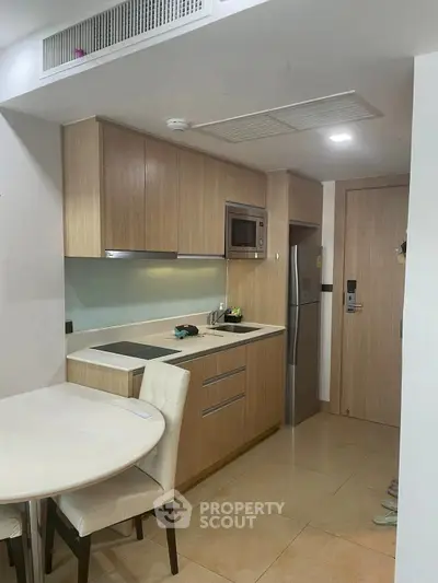 Modern compact kitchen with wooden cabinets and dining area in cozy apartment.