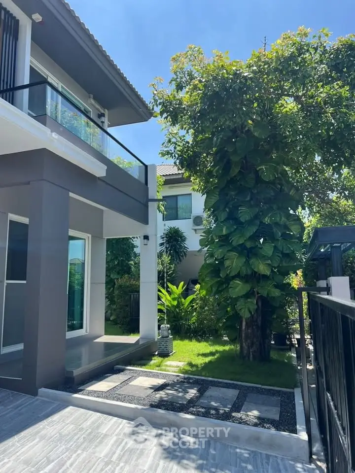 Modern two-story house with lush garden and spacious driveway under clear blue sky.