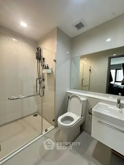 Modern bathroom with glass shower, sleek fixtures, and large mirror in a contemporary apartment.