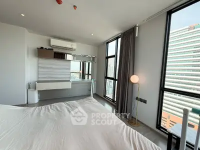 Modern bedroom with large windows offering city views, featuring sleek design and ample natural light.