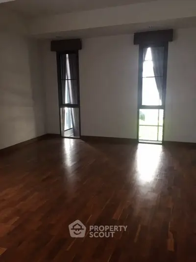 Spacious empty room with wooden flooring and large windows for natural light.