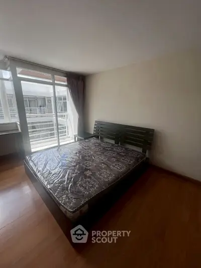 Spacious bedroom with large window and wooden flooring in modern apartment.